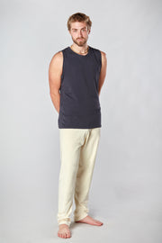 Man with beard facing forward with hand behind his back wearing a cream color pair of organic cotton Mana yoga pants