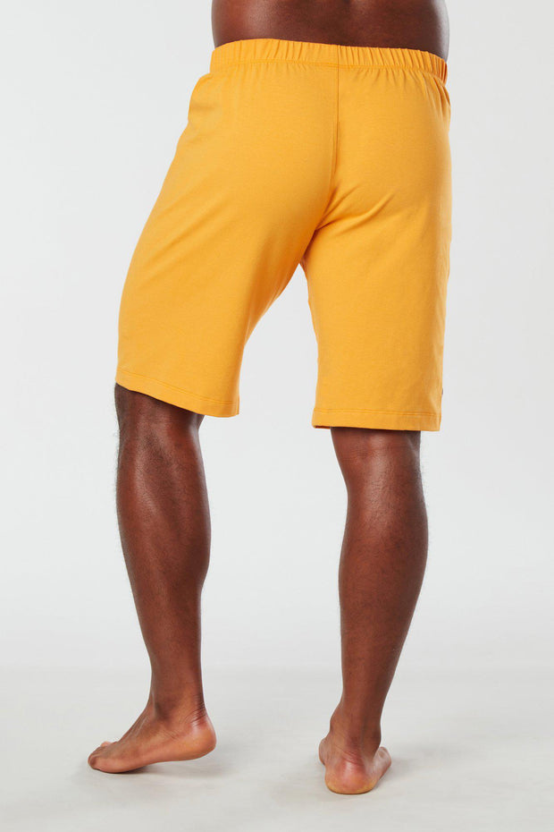 Back of mans lower half of body wearing yellow colored organic cotton Mana yoga shorts