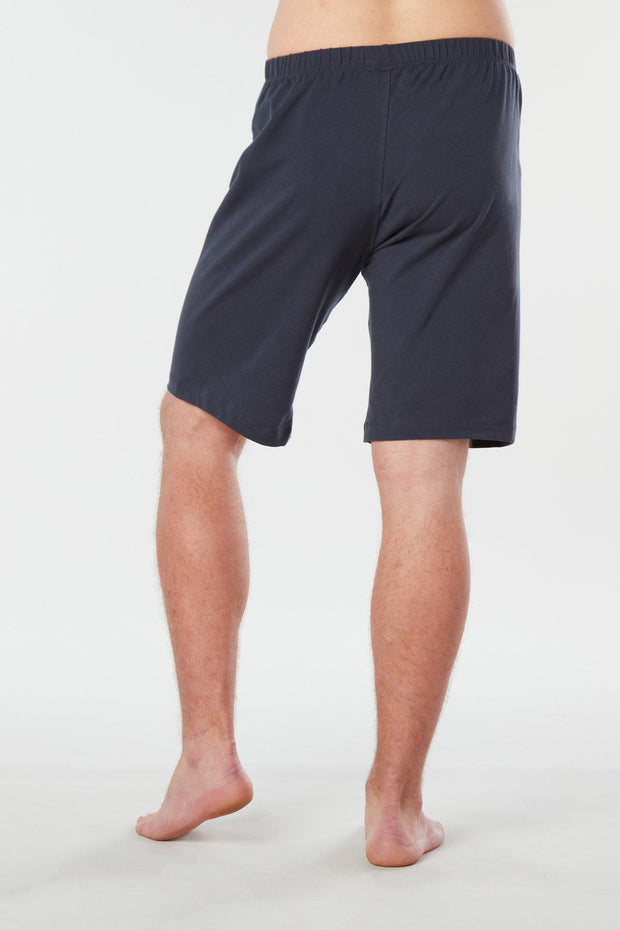 Back of mans lower half of body wearing midnight blue colored organic cotton Mana yoga shorts