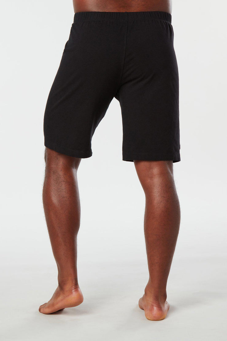Back of mans lower half of body wearing black colored organic cotton Mana yoga shorts