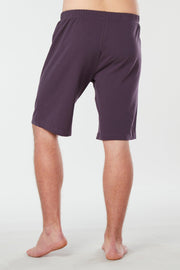 Back of mans lower half of body wearing purple colored organic cotton Mana yoga shorts