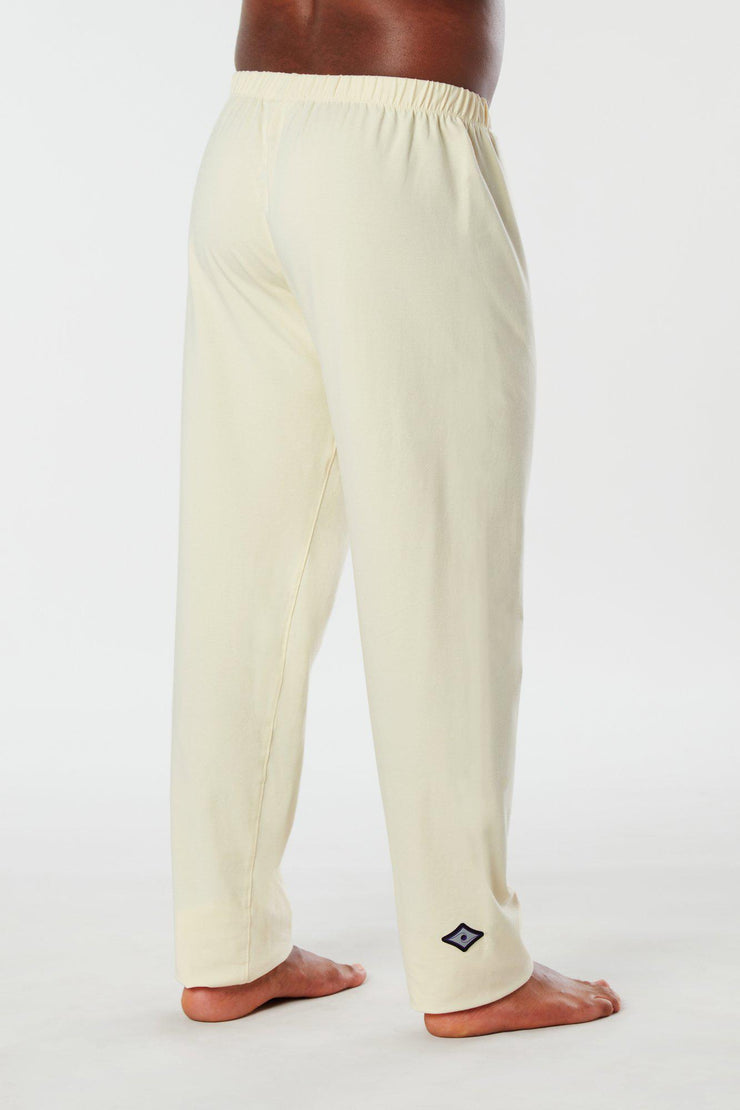 Man standing with side and back view of cream colored organic cotton Mana yoga pants