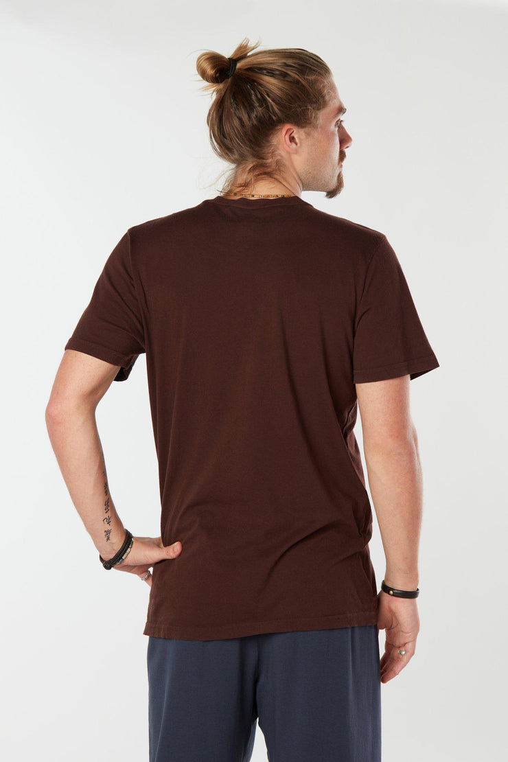 Man facing backward with one hand on his hip wearing dark chocolate colored organic cotton Mana Tee yoga shirt