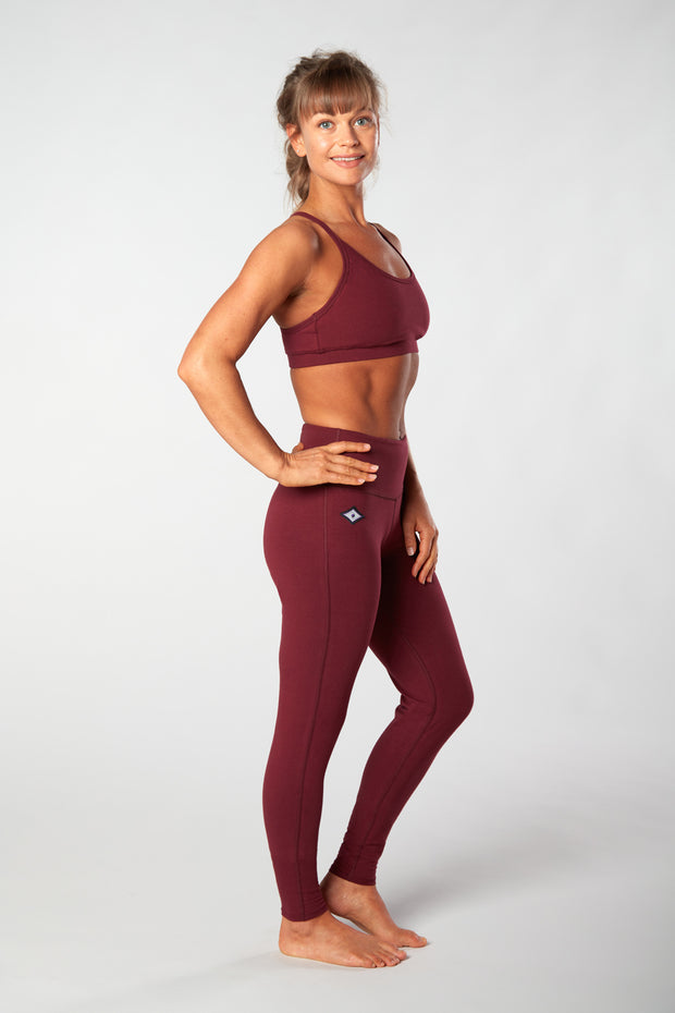 Woman facing sideways smiling with hand on hip wearing maroon organic cotton Luana Legging yoga pants