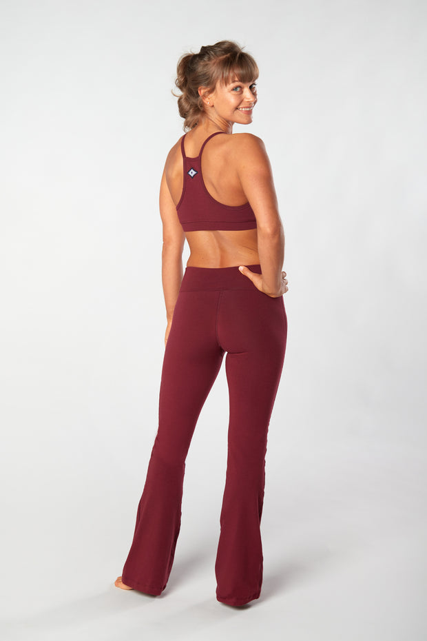 Woman facing away looking over her shoulder smiling with her hand on her hip wearing color matching sports bra and organic cotton Moana Yoga Pants
