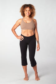 Women facing forward smiling with her hand on her hip wearing a black colored organic cotton Moana Capri yoga pant and tan colored sports bra