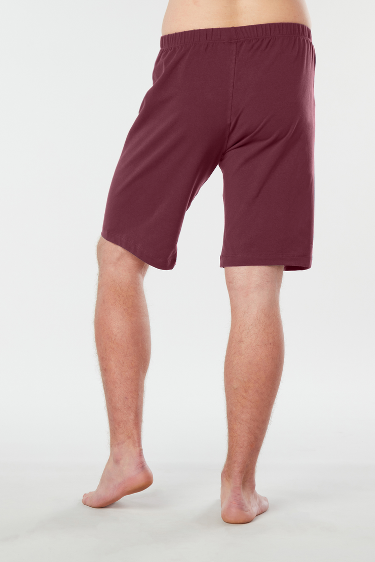 Back of mans lower half of body wearing maroon colored organic cotton Mana yoga shorts