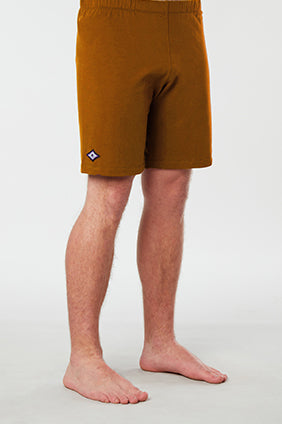 Front facing mans lower half of body wearing mustard colored organic cotton Mana yoga shorts